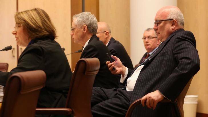 Attorney-General Senator George Brandis (right) checks his phone during the Senate budget estimates hearing with PM&C officials at Parliament House on Monday. Photo: Andrew Meares