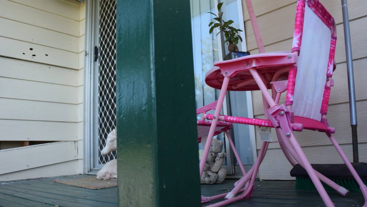 A children's table and chairs sits on a verandah peppered with bullet marks. Picture: Angela Thompson