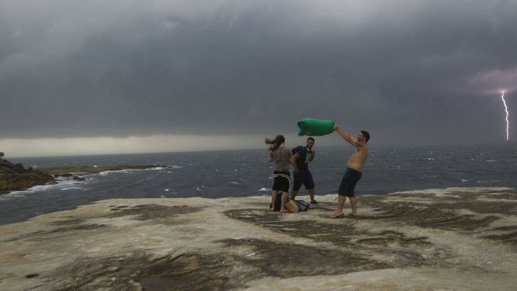 Beachgoers brace against the wind as lightning strikes in the background. Photo: Sahlan Hayes