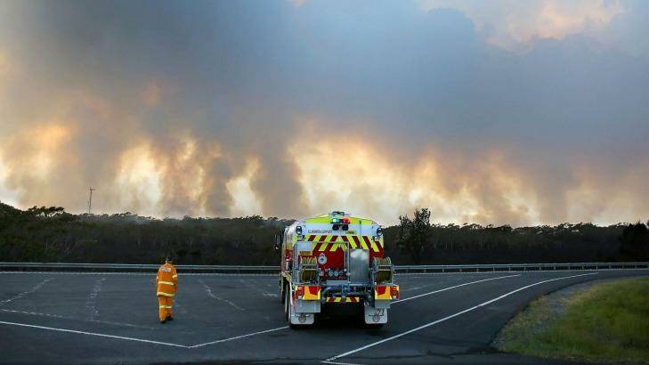 A Rural Fire Service volunteer stands beside his tanker on the M1 motorway watching a bushfire on Maddens Plain on the Illawarra Escarpment.  Photo: Kirk Gilmour