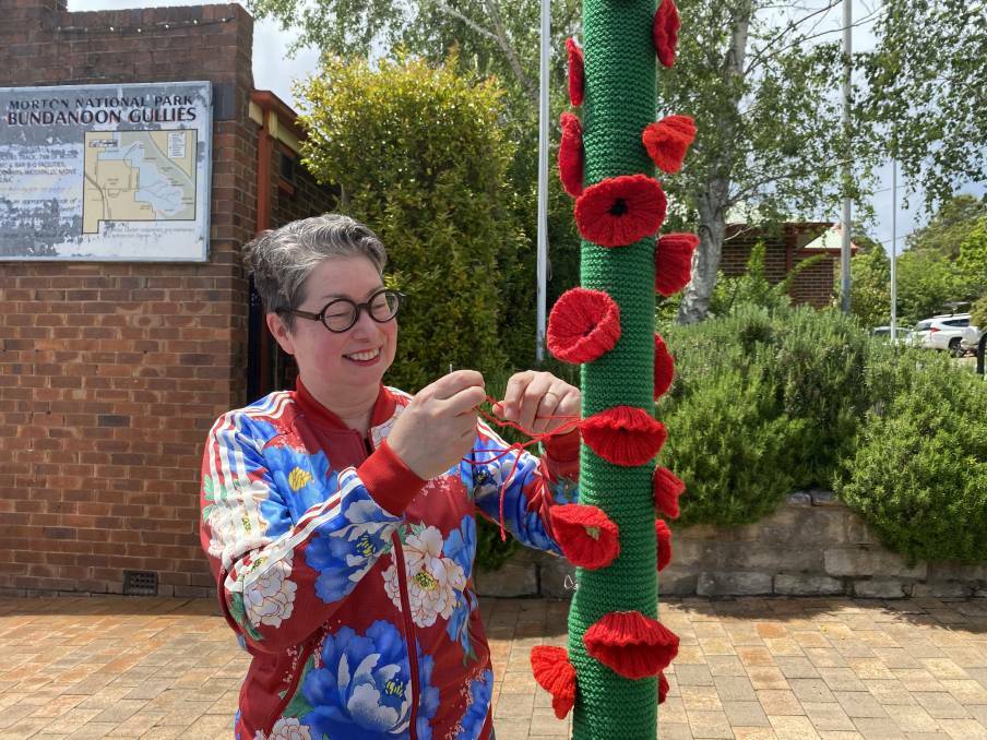 Alison Ayers, also known as Kitty Knitter is securing a wrap covered in poppies for Remembrance Day to a pole in Bundanoon. Picture: Briannah Devlin 