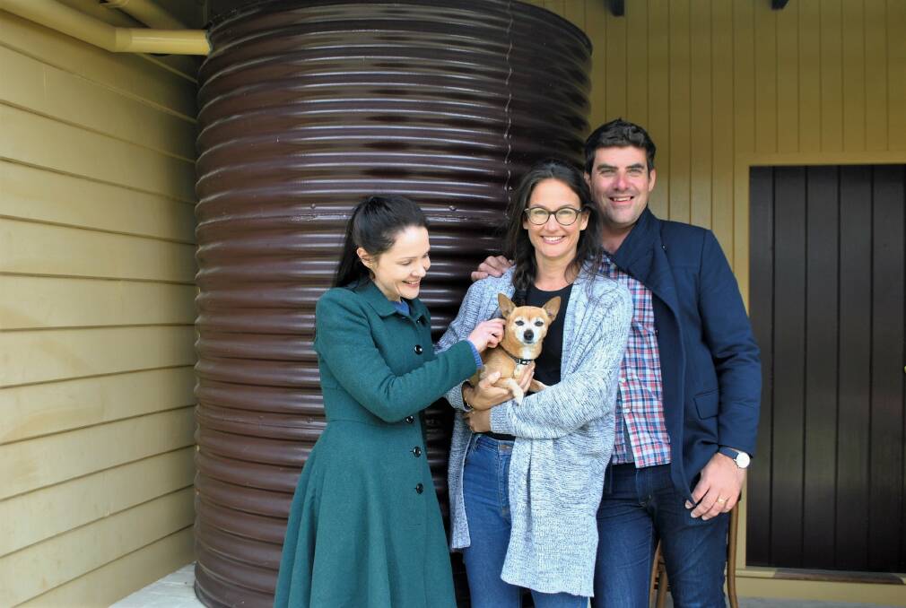 LAST STOP: Russell and Lauren Torrance, their dog Wolfy, and Greta Bradman stand in front of the water tank that her grandfather Sir Donald Bradman used to bounce balls off during cricket practice. Photo: Charli Shield. 