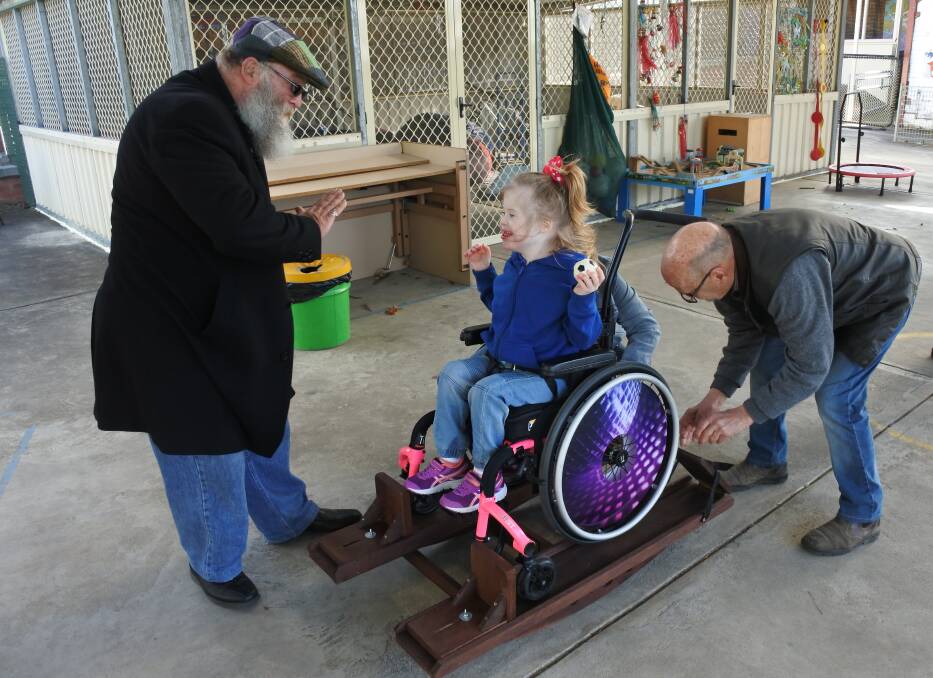 SEE-SAW: Tangara student Lilah Fowler puts the handmade rocker, presented by Moss Vale Men’s Shed President Richard Milne and member Alan Barnes, to the test. Photo: Charli Shield. 