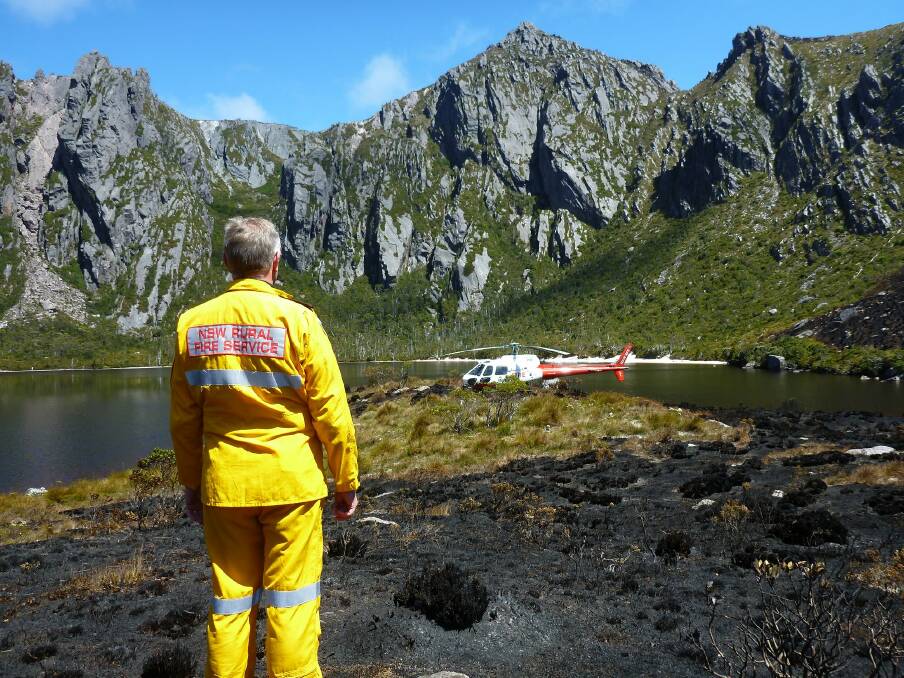 CALL OF DUTY: NSW Rural Fire Service firefighter Andrew McDonald looks out at a RFS helicopter near Reeds Peak behind Lake Rhona in Tasmania. Photo: Supplied