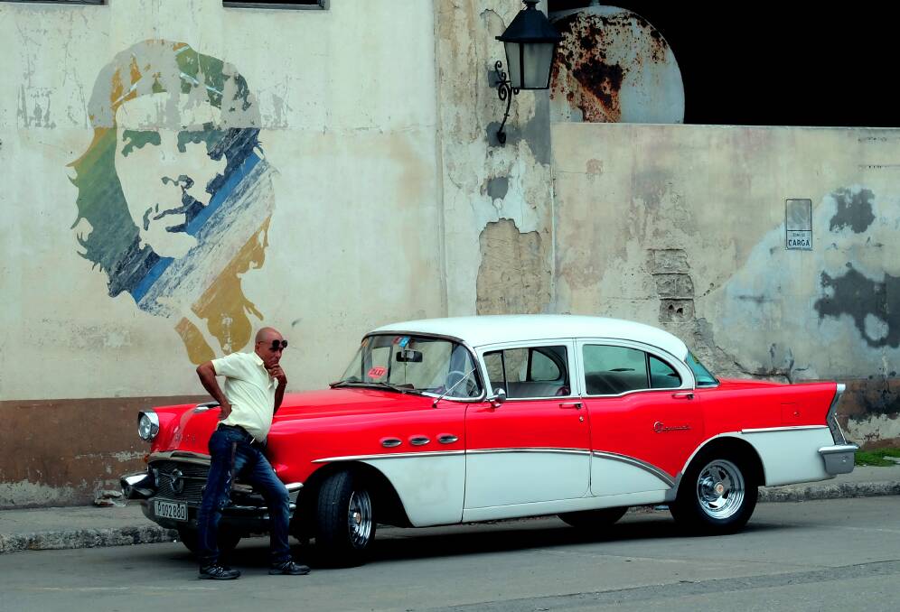 TAKEN FOR A RIDE: Cuban cabbie with his superb 1955 Buick, as an image of Che Guevara looks on. 
