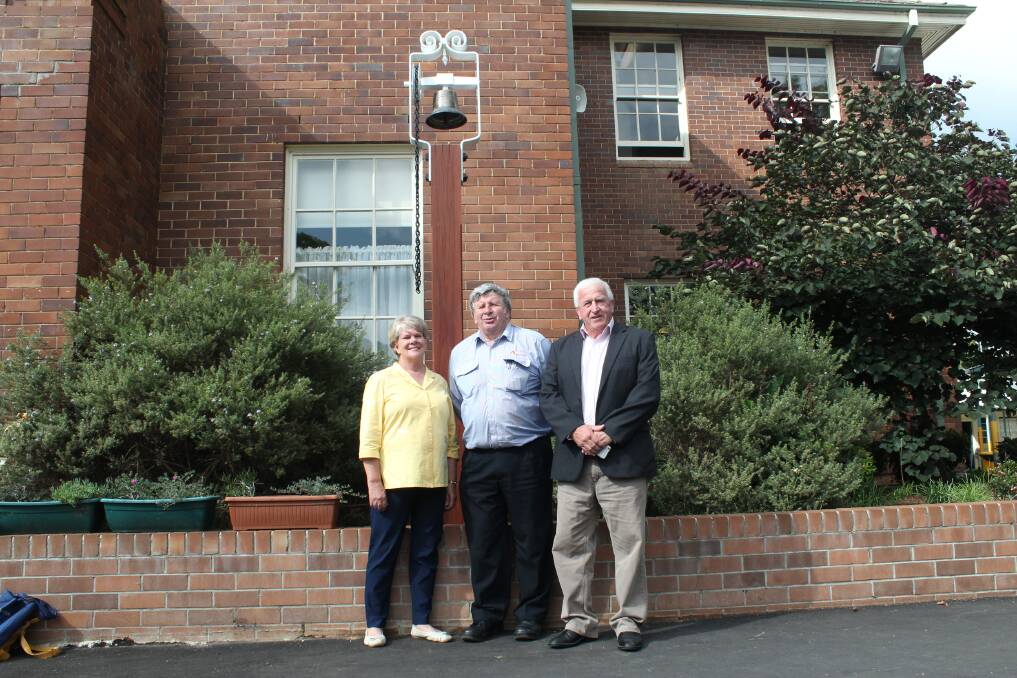 Ann Dawes with Kevin Andrews and Grahame Andrews in front of the newly refurbished bell at Mittagong Public School. 	Photo by Megan Drapalski