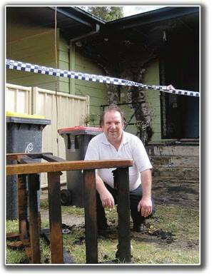 Moss Vale resident Michael Dahms outside his fire damaged home with the remains of the porch chair where the fire started. A smoke alarm woke the Dahms in time to allow them to escape the house and call firefighters.